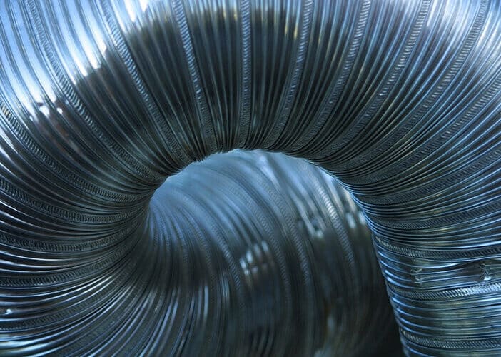 4 Benefits Of Custom Sheet Metal Ductwork Services | Solace Plumbing, Heating, And Air Close-Up Of Custom Sheet Metal Ductwork Forming A Loop. The Ribbed Texture And Silver Color Are Prominent, With Light Reflecting On Its Surface, Showcasing The Craftsmanship And Benefits Of Professional Services.
