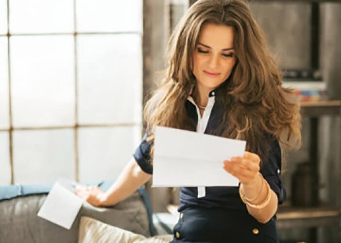 What Are High-Velocity Mini-Duct Ac Systems? | Solace Plumbing, Heating, And Air A Woman With Long Hair Reads A Piece Of Paper, Comfortably Seated In A Room Equipped With Energy-Efficient High-Velocity Mini-Duct Ac Systems. Sunlight Streams Through The Window, Casting Soft Shadows On The Shelves Lining The Walls.