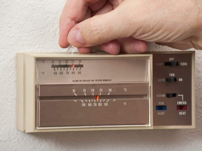 6 Hvac Issues That Plague Older Homes In Brentwood, Tn | Solace Plumbing, Heating, And Air Hand Adjusting An Analog Thermostat On A Wall In Brentwood, Tn, Showing Fahrenheit And Celsius Scales, With Heating And Cooling Mode Options—Ideal For Tackling Common Hvac Issues Found In Older Homes.