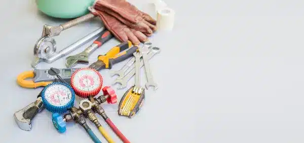 A selection of plumbing tools, from wrenches to gloves and pressure gauges, is neatly arranged on a light surface, ready for the next Nashville, TN air conditioning repair.