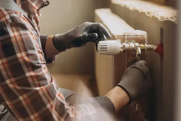 In Nashville, a person wearing gloves carefully adjusts a radiator valve indoors, ensuring optimal comfort and climate control.