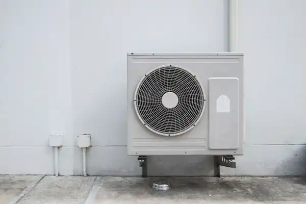 Wall-mounted outdoor heat pump installation with visible pipes, set against a plain white wall and concrete floor in Nashville, TN.