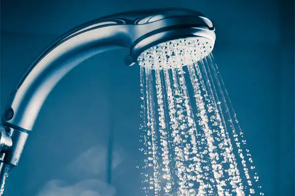 Close-up of a showerhead with water streaming down, reflecting the efficiency of a tankless water heater against a dark blue background.