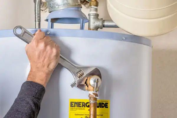In Jackson, TN, a person uses a wrench to adjust a fitting on a water heater. An EnerGuide label is visible on the heater, emphasizing efficiency and expert water heater repair.