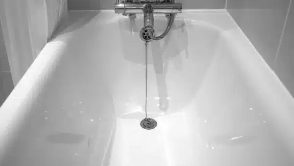 A White Bathtub With A Chrome Faucet And A Drain Plug On A Chain In The Center.